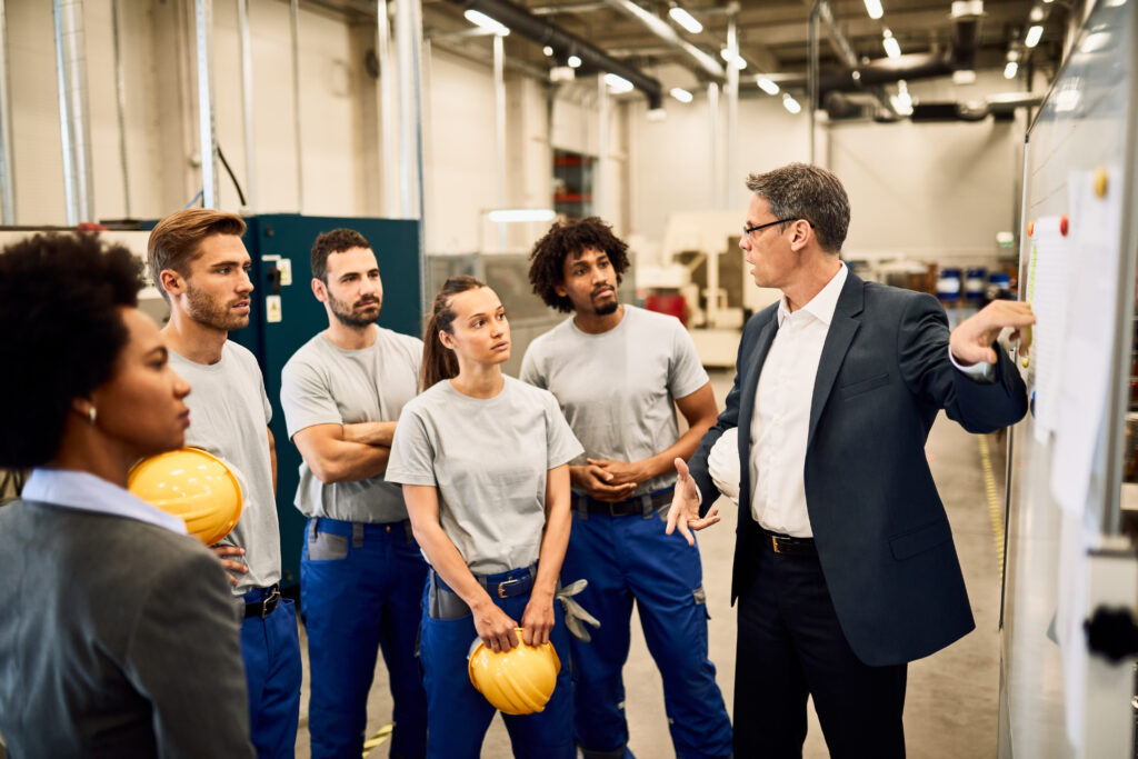 empresario adulto medio dando apresentacao ao grupo de trabalhadores industriais em uma fabrica